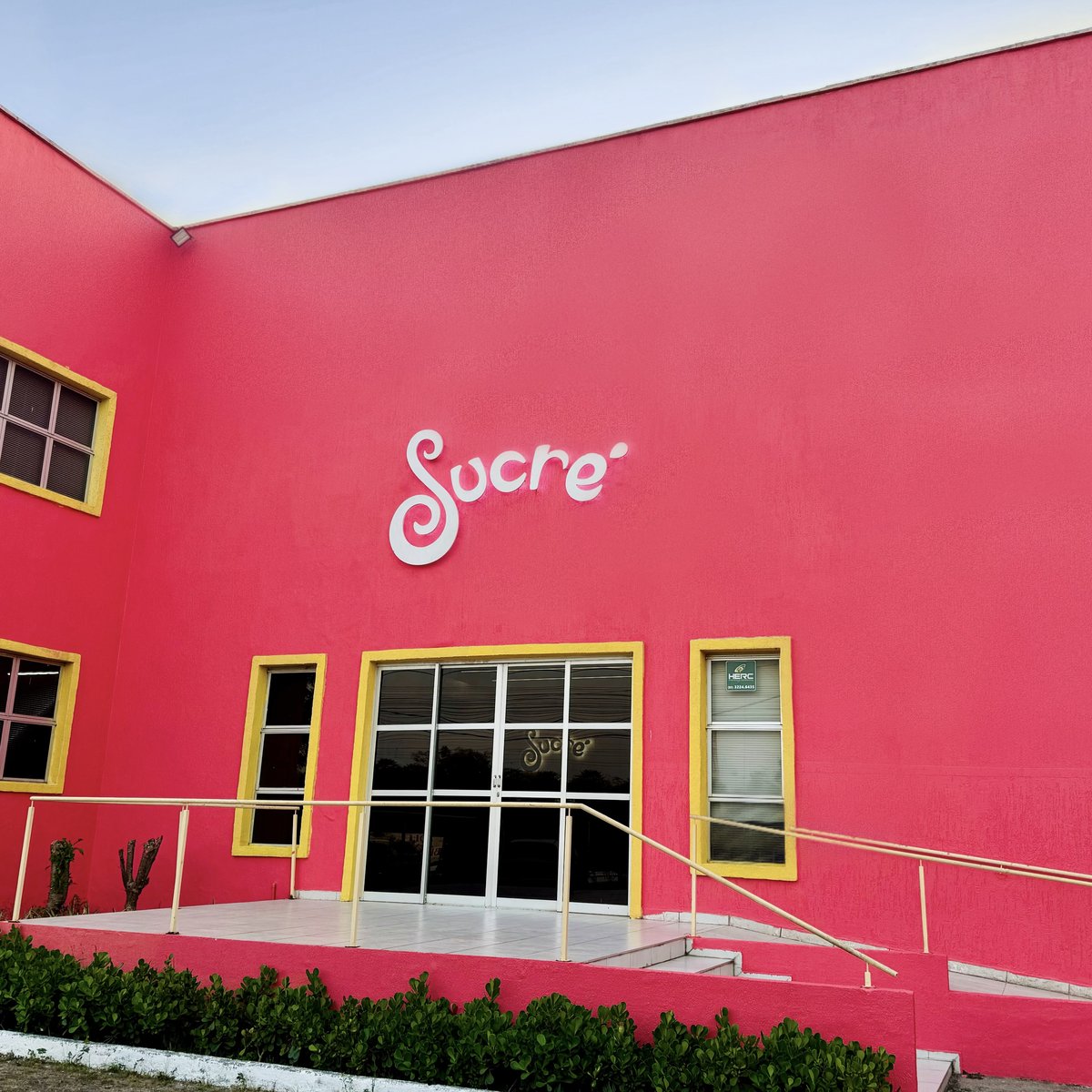 Fachada rosa da fábrica da Sucré com janelas amarelas e o logo na parede