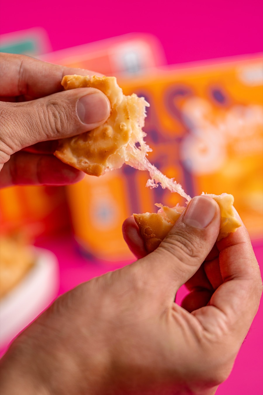 Mãos partindo um mini pastel Sucré crocante com o queijo derretido esticando entre as metades